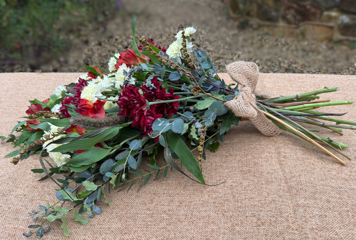 Red and white winter funeral sheaf with chrysanthemums, alstroemeria, eucalyptus and grasses, tied with a raffia bow, Tunbridge Wells.